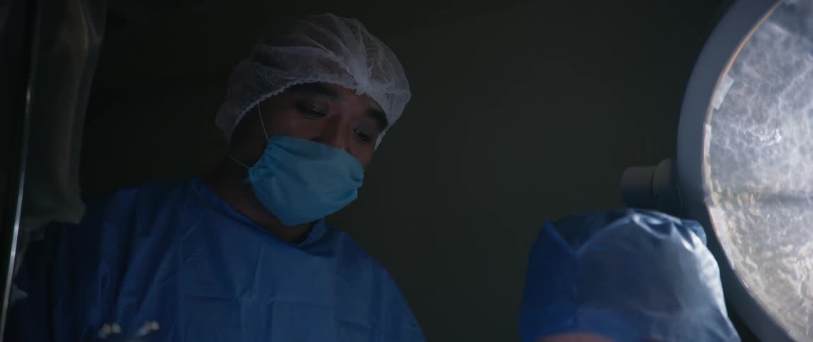 Two medical professionals look down at something while wearing personal protection gear