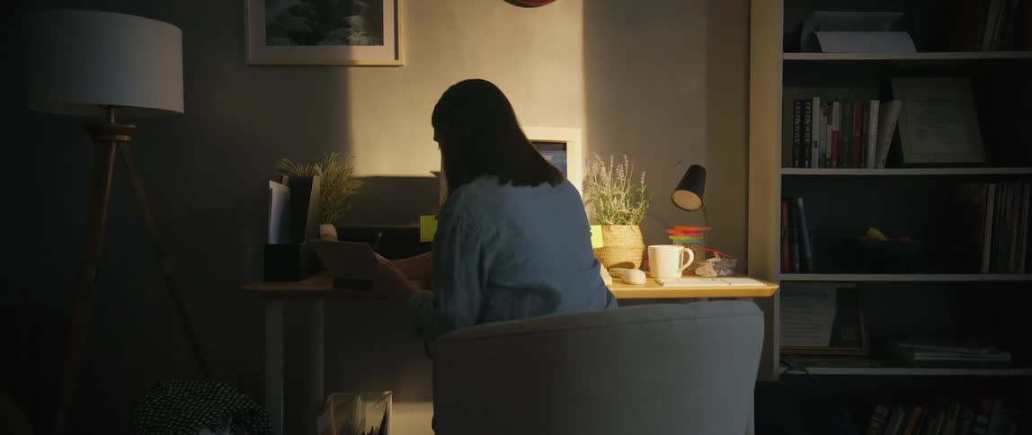 A woman sits in a chair at her desk and begins writing in a notebook