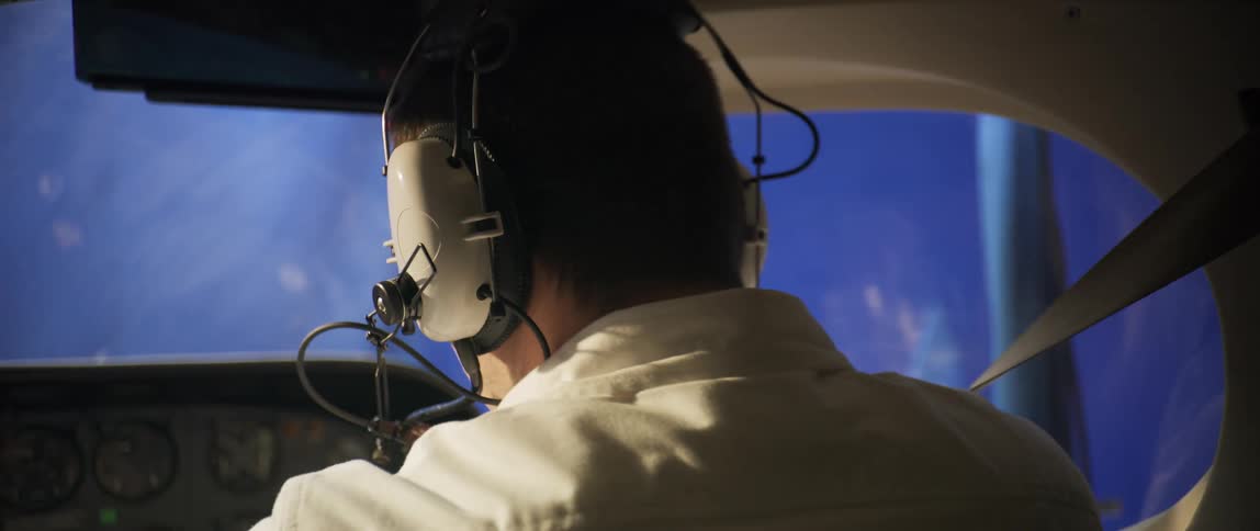 A pilot sits at the cockpit and wears his seatbelt and headphones