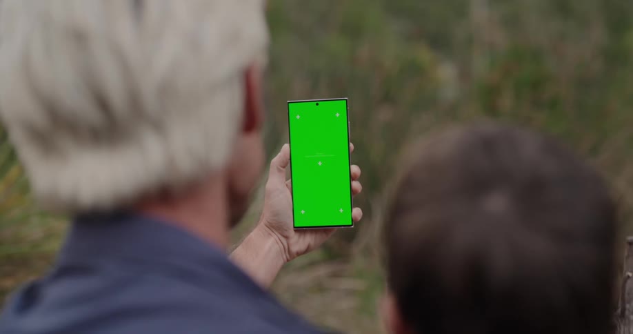 Man holding a cell phone with a green screen as his young son stands next to him