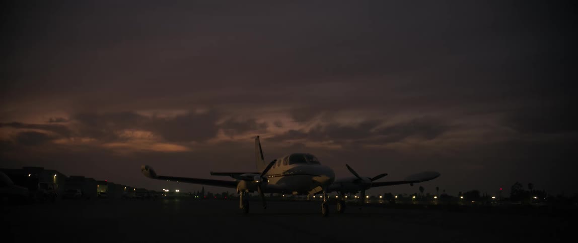 Small plane parked on an airport runway against a dark cloudy sky