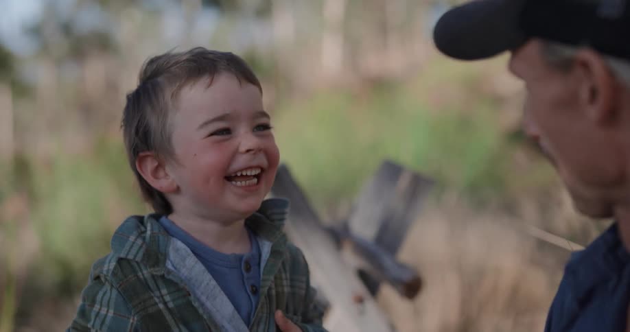 A boy laughs and points at a man who is making faces at him