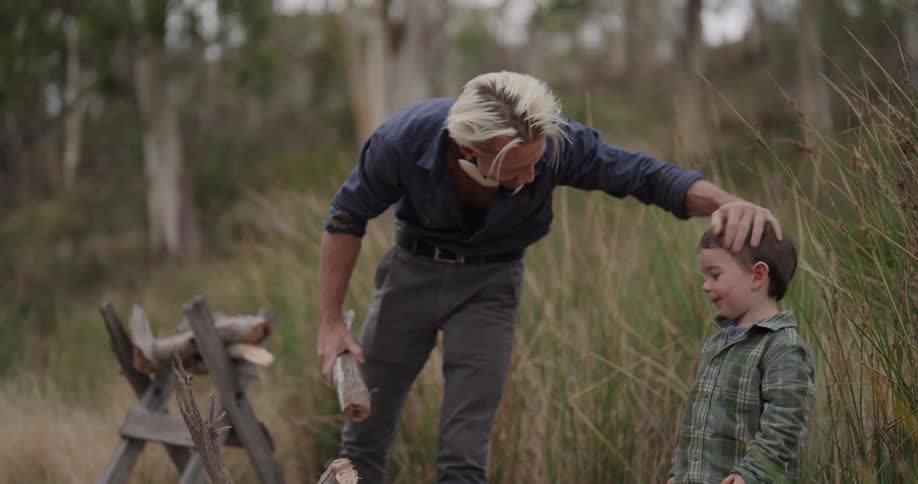 Boy handing a piece of wood to his father who pats his head