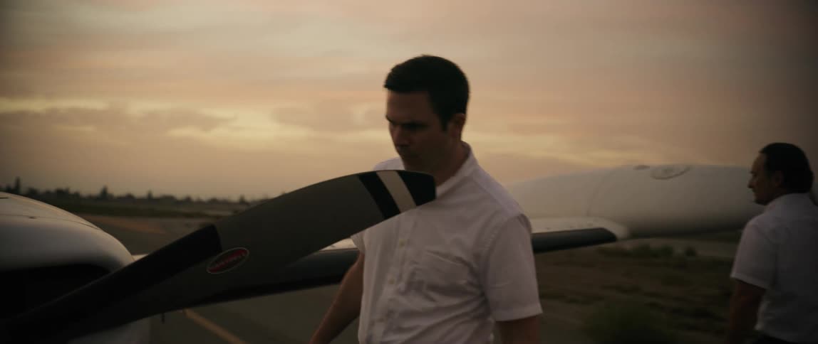 Two men checking out an airplane on the runway in the evening