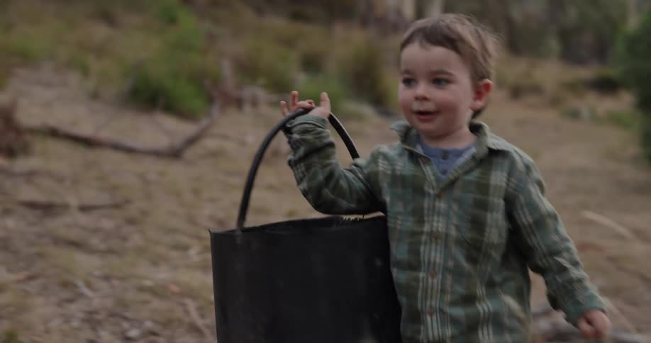 A child carries a bucket by the trees