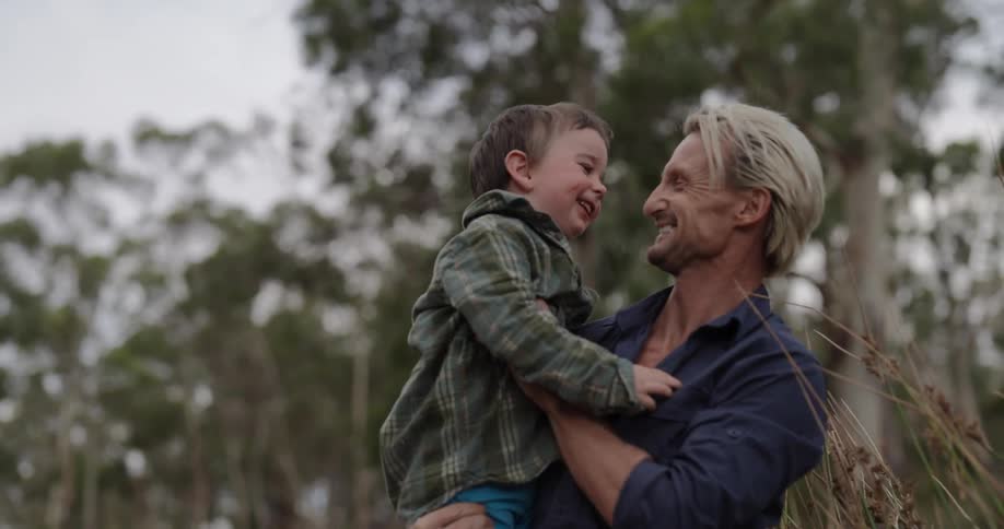 A father holding his son in his arms hugging and smiling outdoors