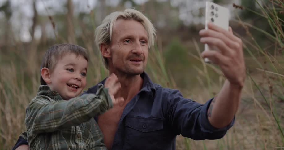 A father holds his son while trying to take a selfie with a phone