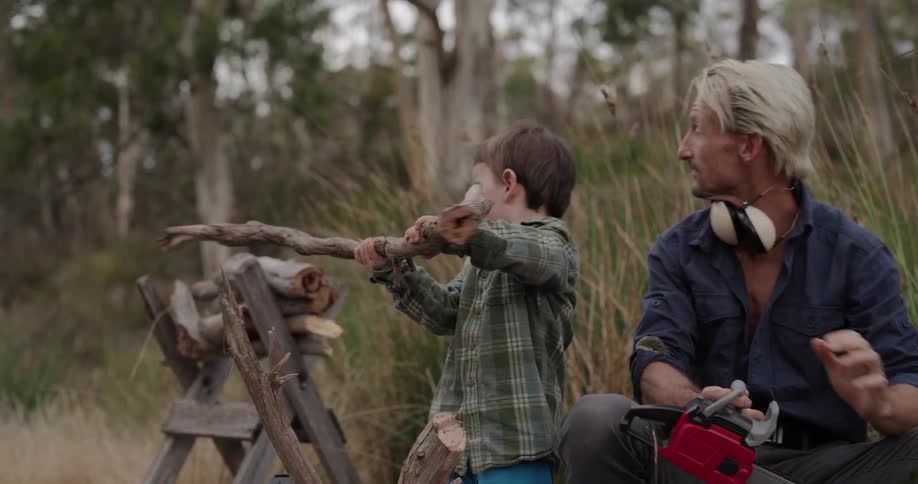 A father and son playing with wood and a toy electric saw outdoors in nature