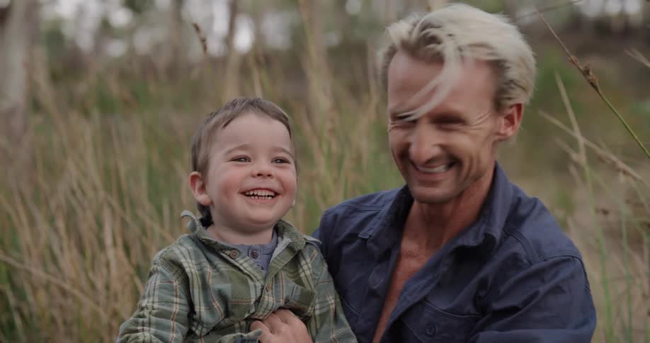 Father and son sitting on the ground outdoors smiling