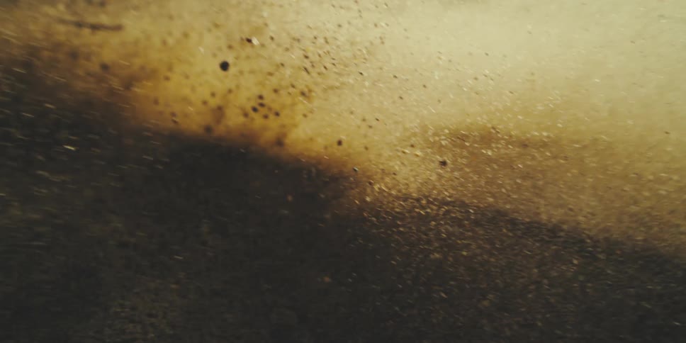 Slow Motion Sand Particles Explode and Drift Through Warm Light