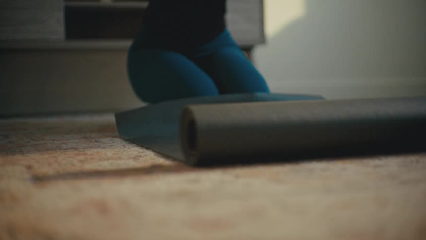 A lady spreads a black mat on the floor indoor at daytime