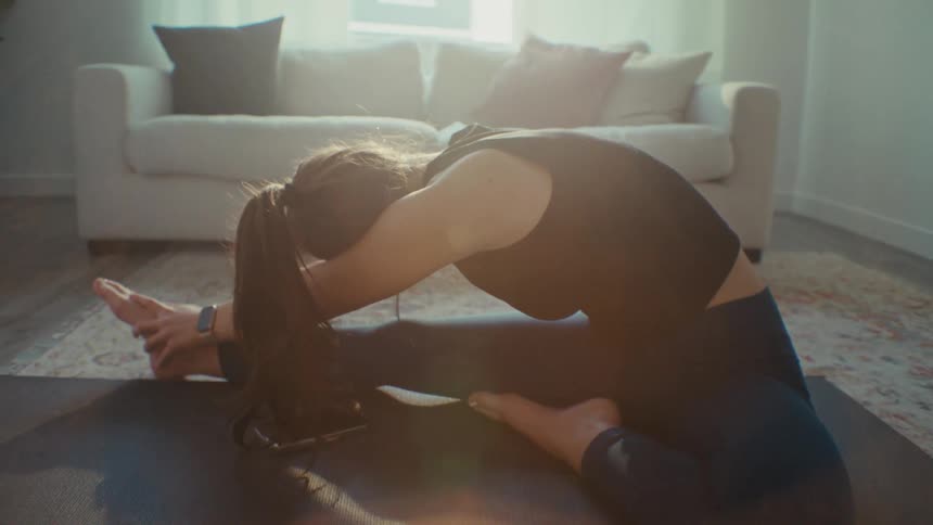 A lady stretches her body in the sitting with sunlight entering through the window at daytime