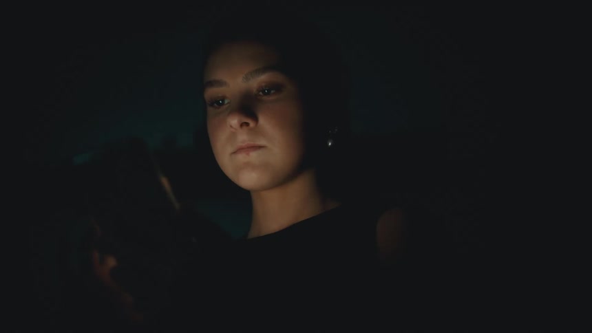 The face of a teenage girl who is fiddling with a cell phone that is shining light on her face