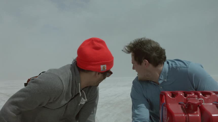 Two men ride on top of a vehicle in the desert