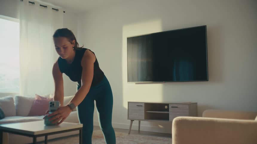 A woman sets up her phone camera and perform a TikTok dance in her living room