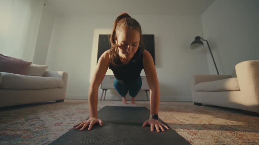 Woman performing burpees with a push up on yoga mat in her living room