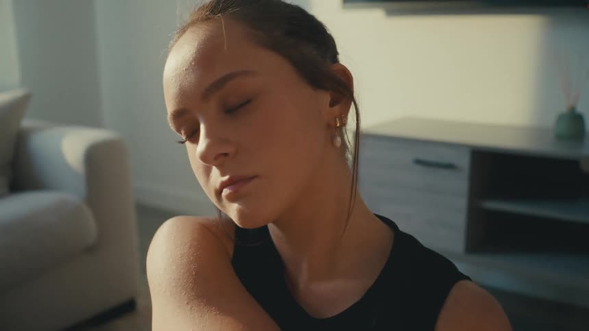 A teenage girl stretches her arms and neck in a living room
