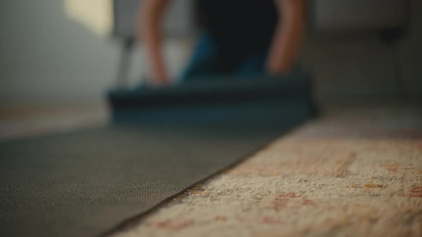 Person rolling out yoga mat on carpet in thier living room