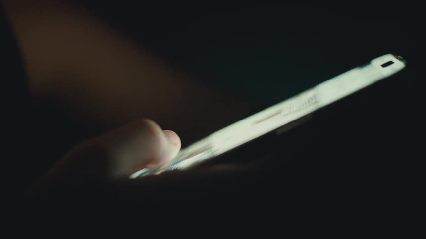 Thumb scrolling through social media on cell phone in the dark