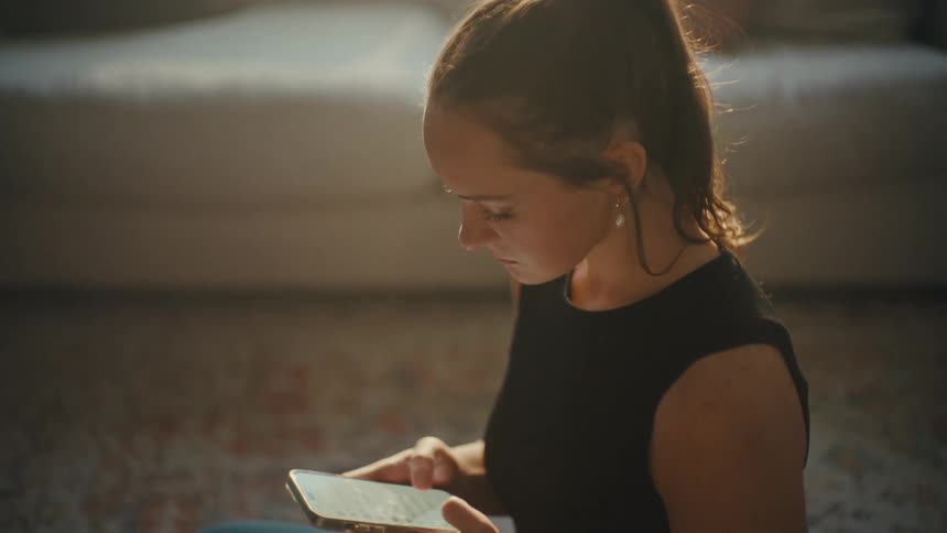 Woman sitting on carpet in her living room texting on cell phone