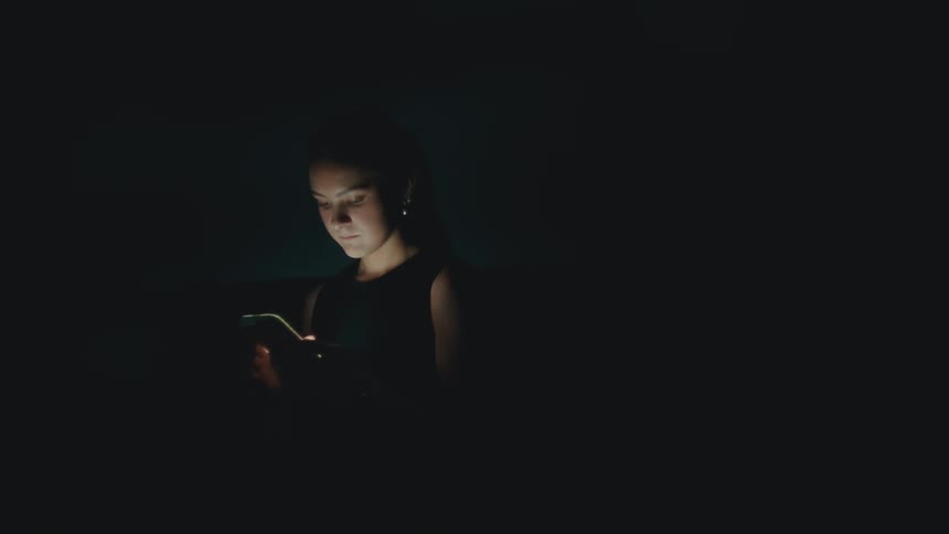 A woman stands in the dark and uses her phone