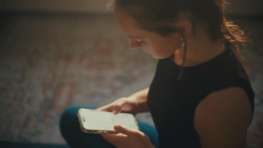 Young lady pressing a mobile phone while sitting in a room at daytime