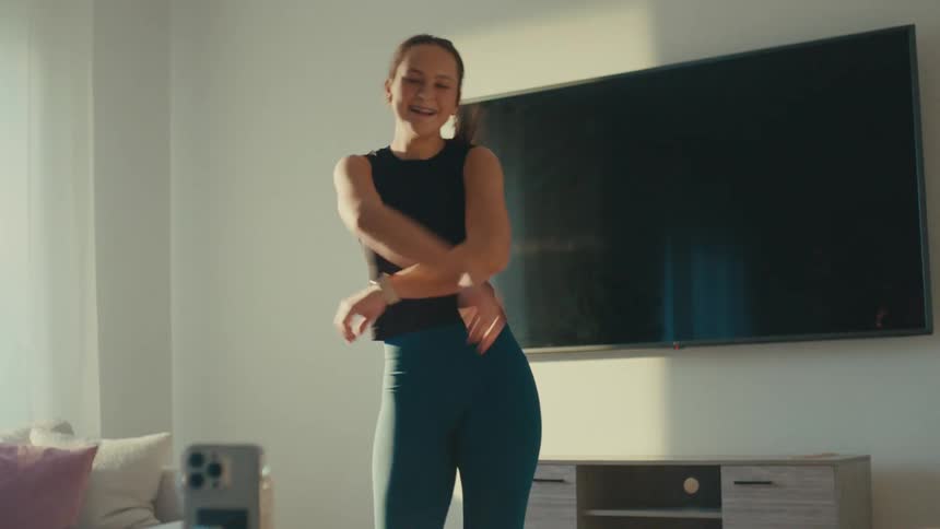 A young woman joyfully dances and films herself with a phone in a bright living room