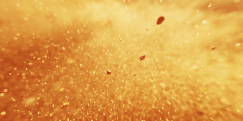 An extreme closeup shows golden particles or atoms exploding or dispersing in super slow motion