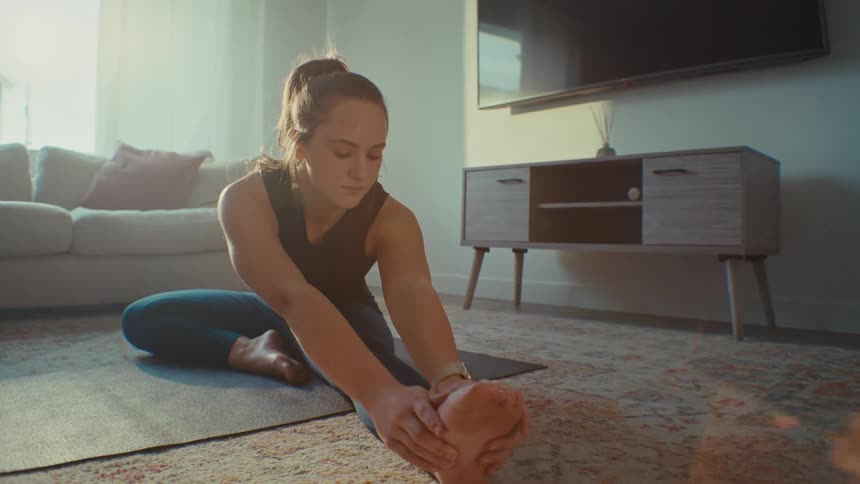 Woman stretching her legs on yoga mat in her living room