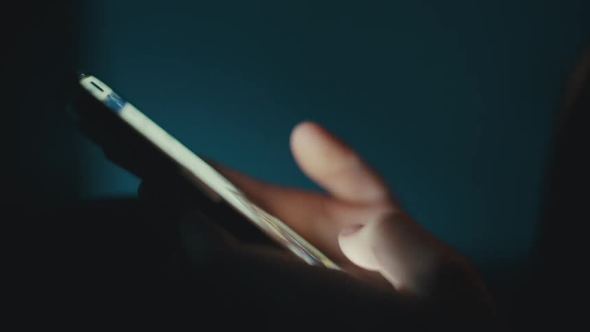 A person is scrolling through photos on their cell phone in a dark room