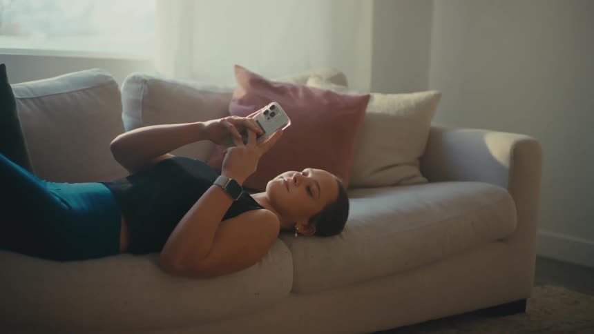 A woman is smiling while using her cellphone on the couch