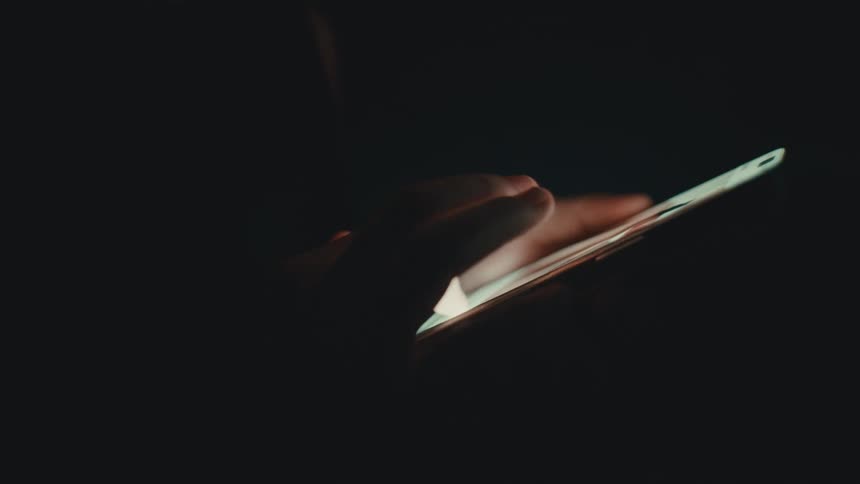 A person is sliding on their phone in the dark
