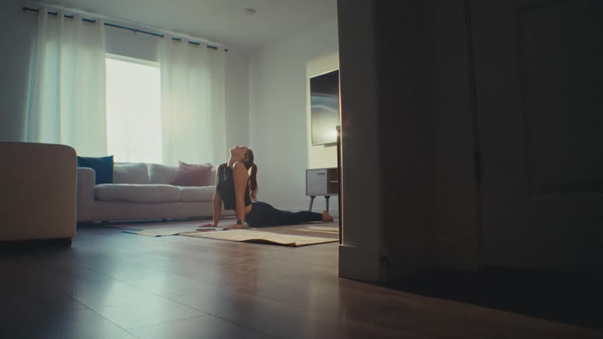 A woman stretches and exercises on a floor mat in a living room