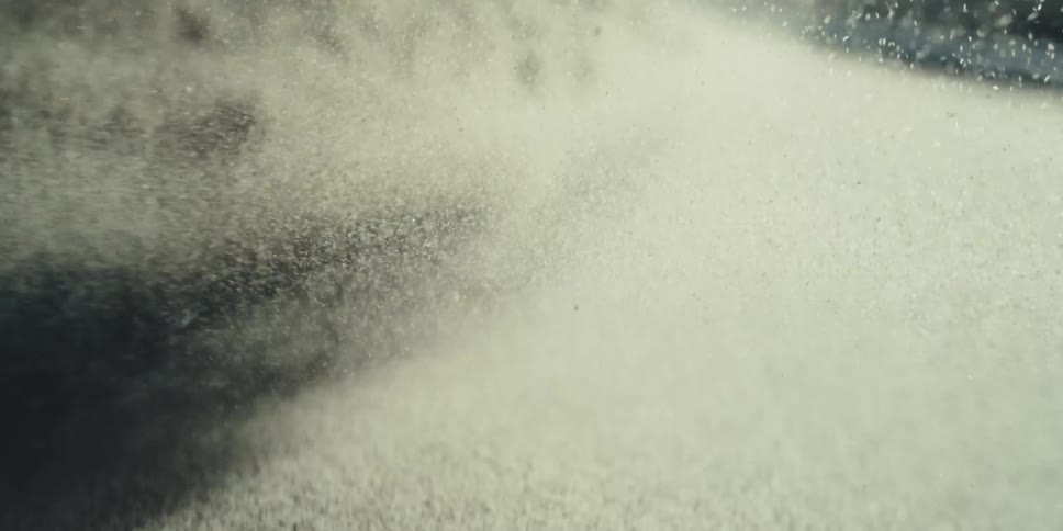 Grains of beach sand float through the water churned by a wave
