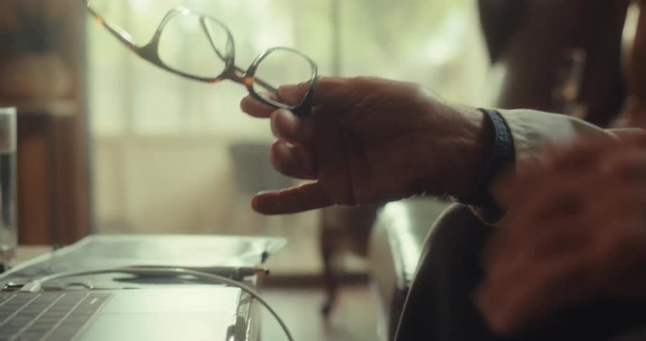 A doctor holding his glasses with a stethoscope next to his laptop on the desk