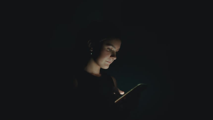 Woman scrolls through a mobile phone in the dark