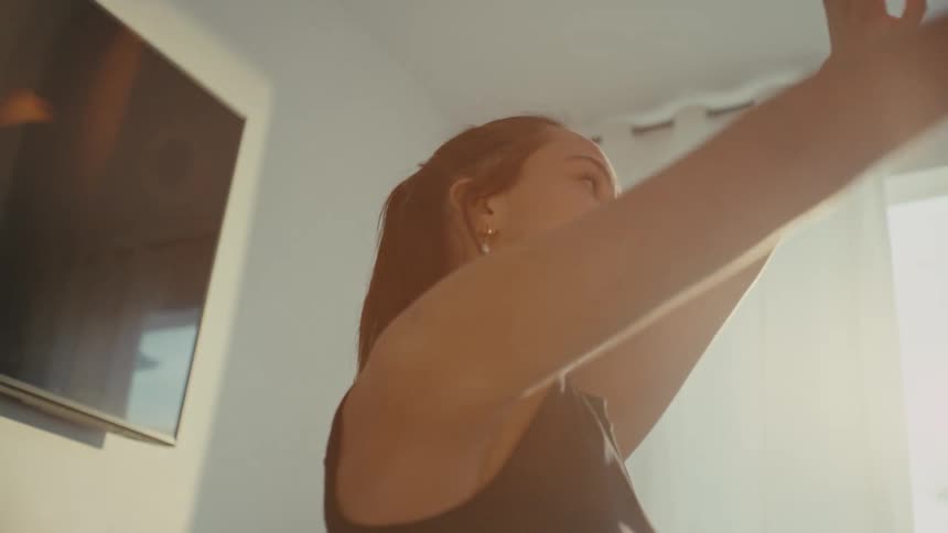 A young woman with her hair tied up stands with her arms up and stretching her neck