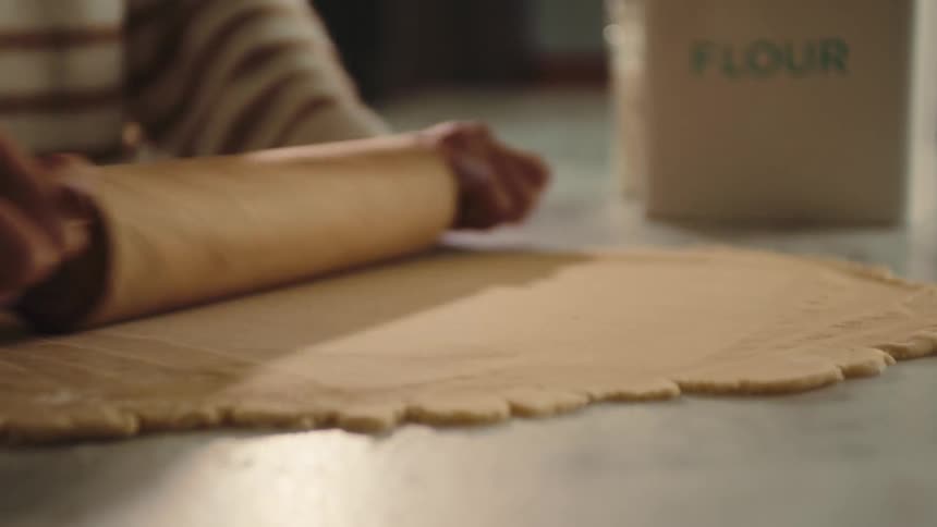 A woman rolls dough on a table top using a wooden rolling pin