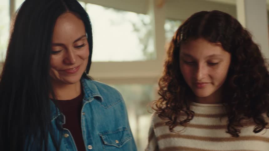 A woman and a teenage girl share a happy sentimental moment together indoors smiling while looking at a handmade bracelet