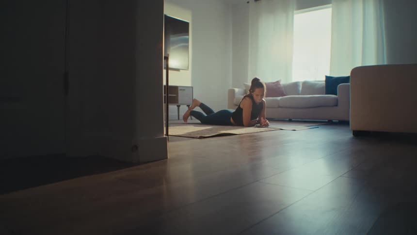 Woman stretching on a yoga mat then scrolling on cell phone in her living room