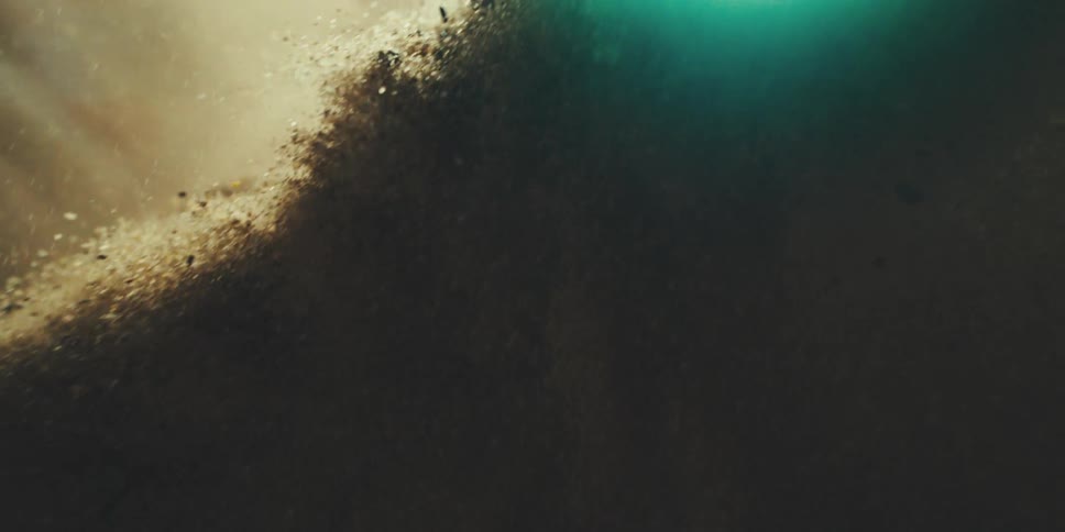 Particles of sand and dust swirl through glowing light in a dark space creating a flowing weightless effect