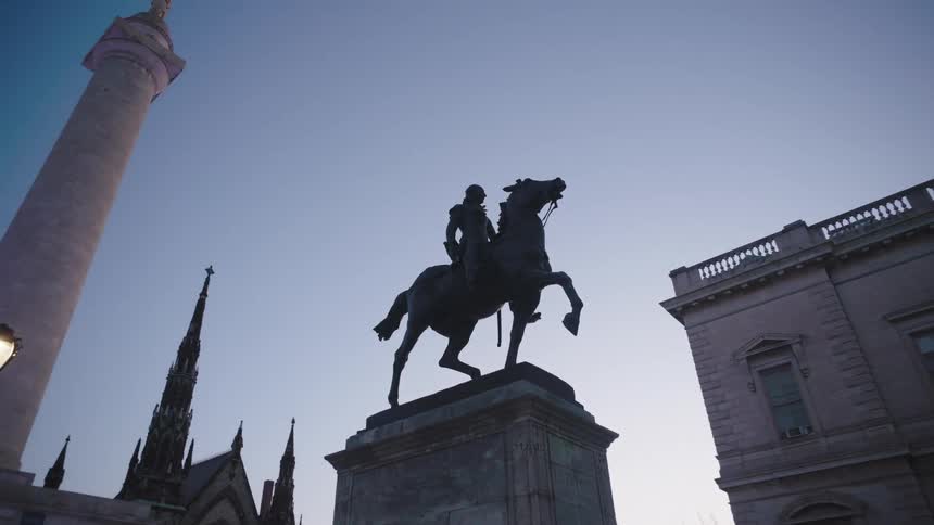 A silhouetted statue of a person on horseback is dramatically framed against a twilight sky with surrounding classical architecture