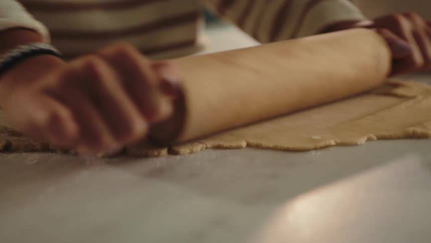 A hand is rolling out a sheet of dough on a marble countertop likely preparing for baking