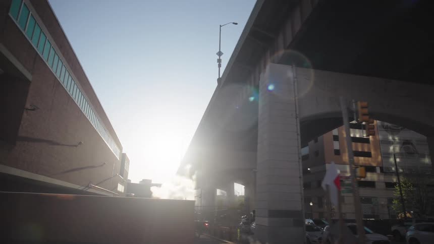 A city underpass is captured with morning light piercing through high concrete overpasses traffic congestion and rising steam contributing to an urban industrial mood