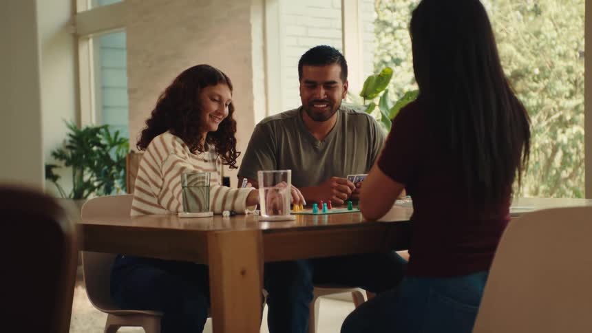 A group of three friends sitting at a wooden table playing a board game happily