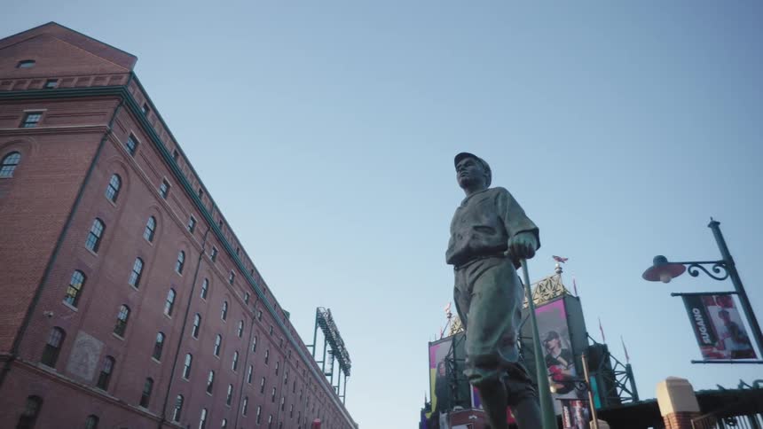 A statue of a baseball player is before the stadium gates