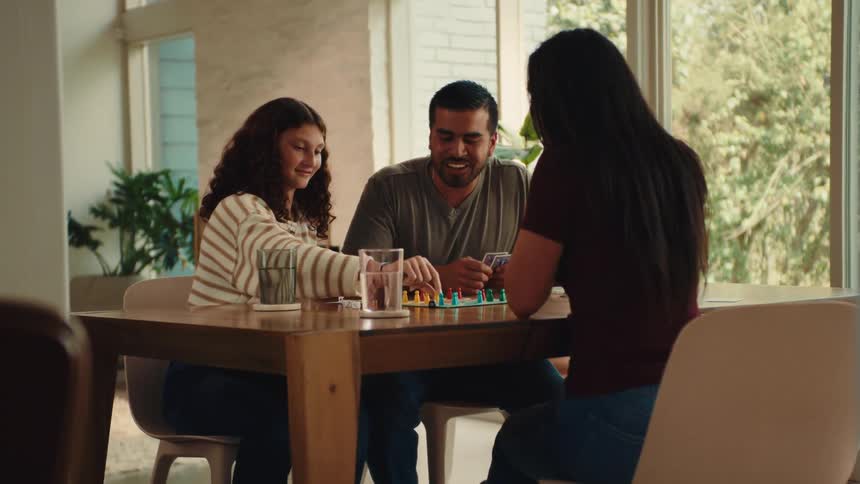 Father and daughter high five each other while a family plays a board game at home