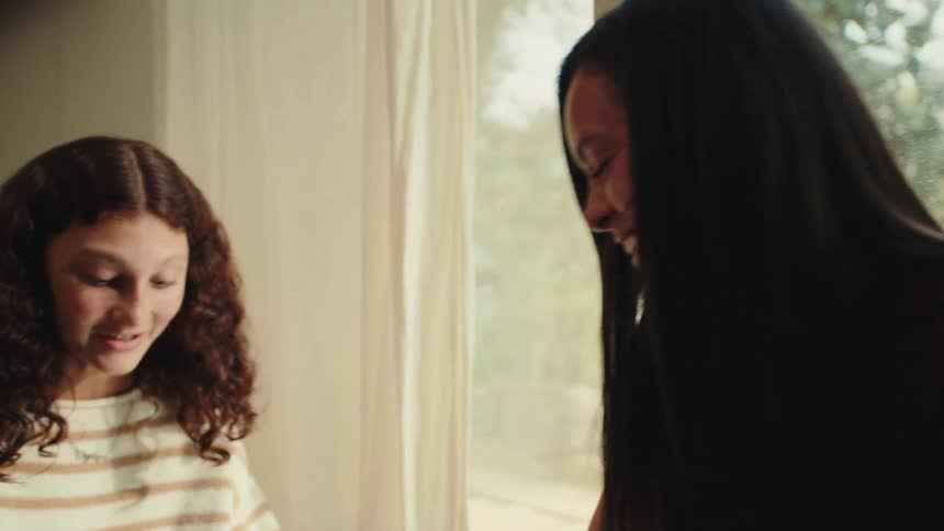 A teenage girl paints another girls fingernails while they laugh indoors