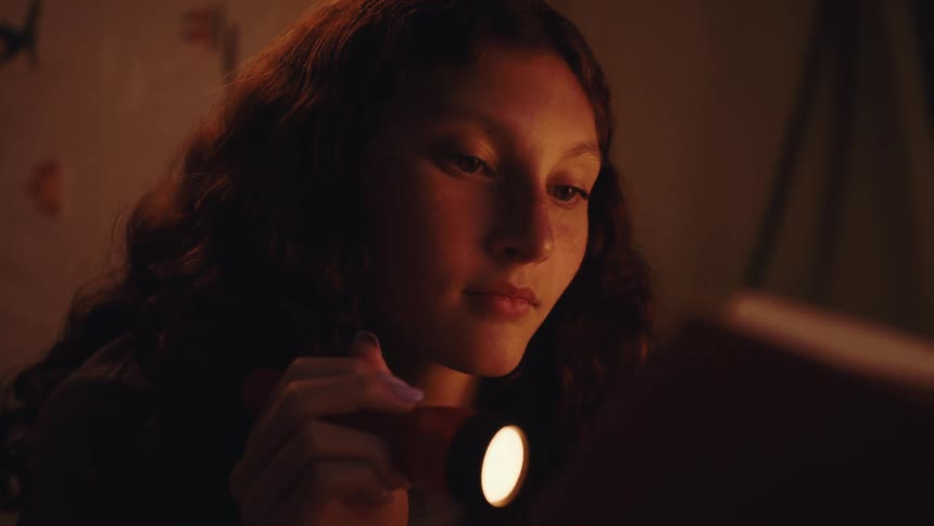 A girl is reading a book with light from a flashlight
