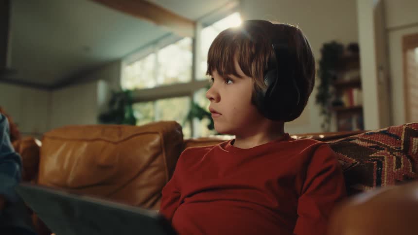 Boy with headphones focused on a tablet and his mother calling